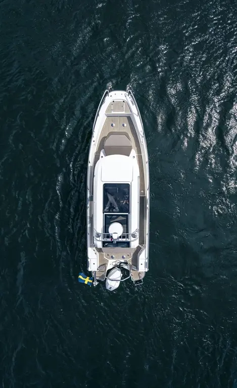 Aerial view of a white motorboat on dark blue water, featuring a Swedish flag and a spacious deck with seating.